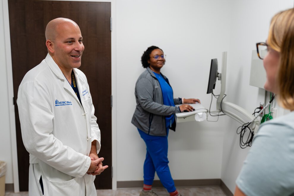 A doctor in an exam room smiles and chats with two nurses.