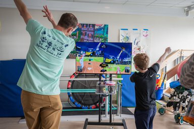 A man and a child play a video game with their arms up in a hospital room.