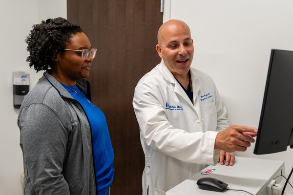A doctor in a white coat points to information on a computer screen to a nurse next to him.