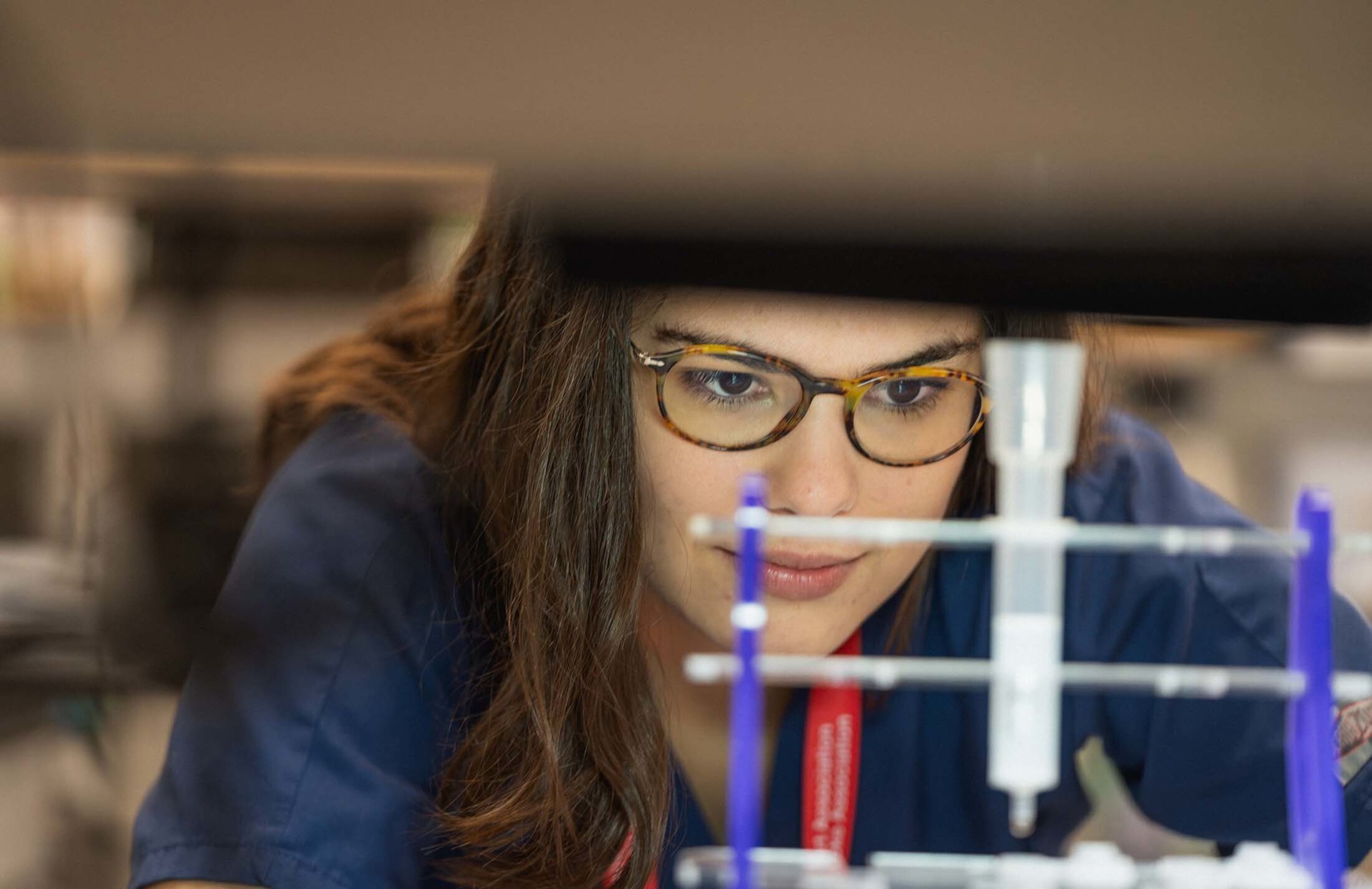 Closeup of a woman's face as she looks at a purple and white stand. She has brown hair and is wearing eyeglasses.