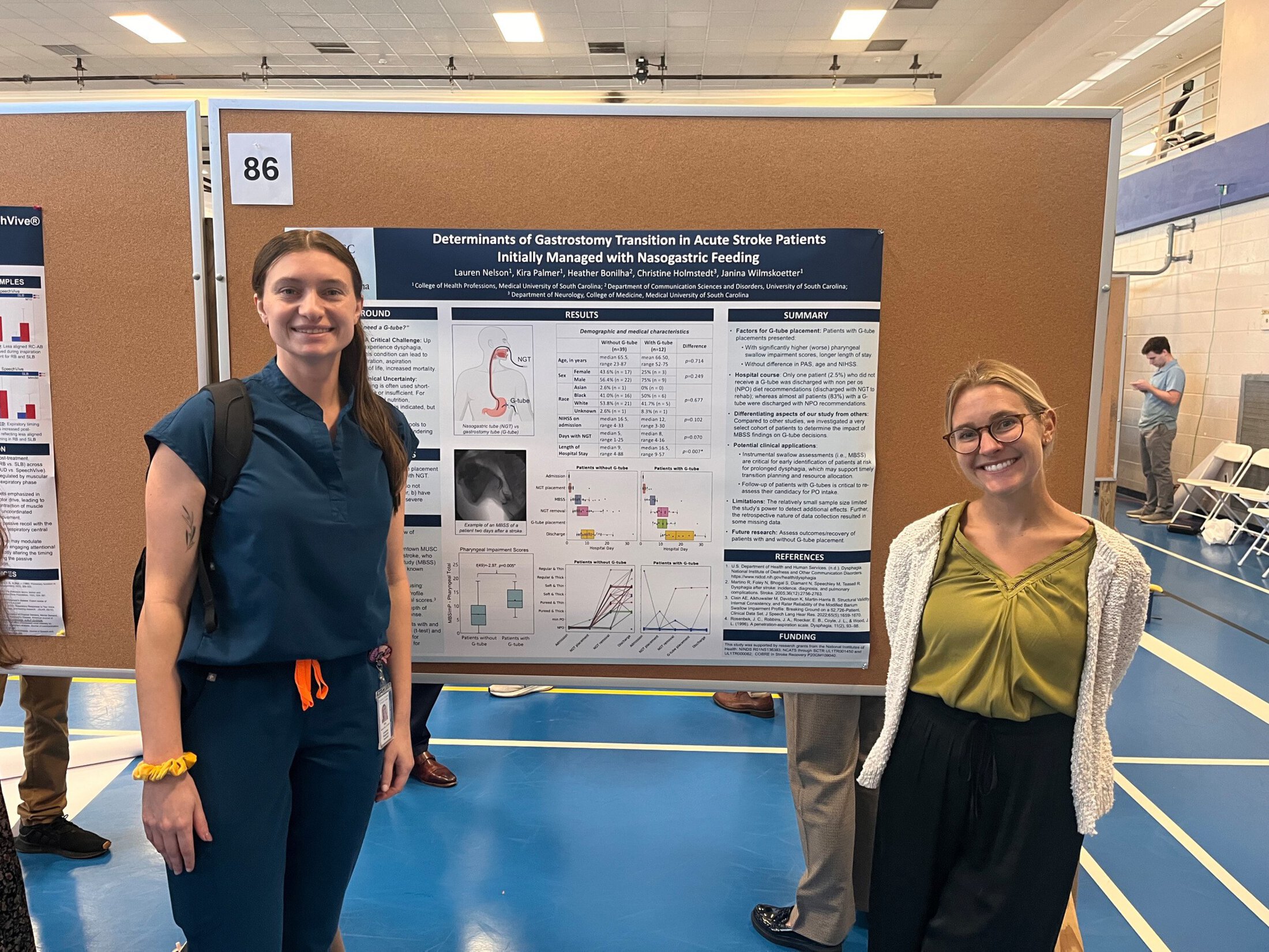 Two women stand in front of a large poster display on a bulletin board.