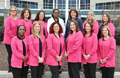 A group photo of a dozen women, most in bright pink jackets.