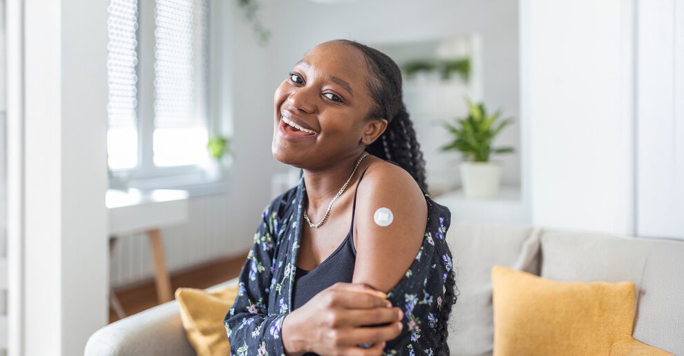 MUSC Health International Travel Clinic Portrait of a female smiling after getting a vaccine. Woman holding down her shirt sleeve and showing her arm with bandage after receiving vaccination.