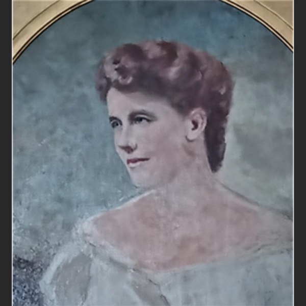 Old photo of a woman with brown hair. She's wearing an off-the-shoulder dress that is light blue or off white.
