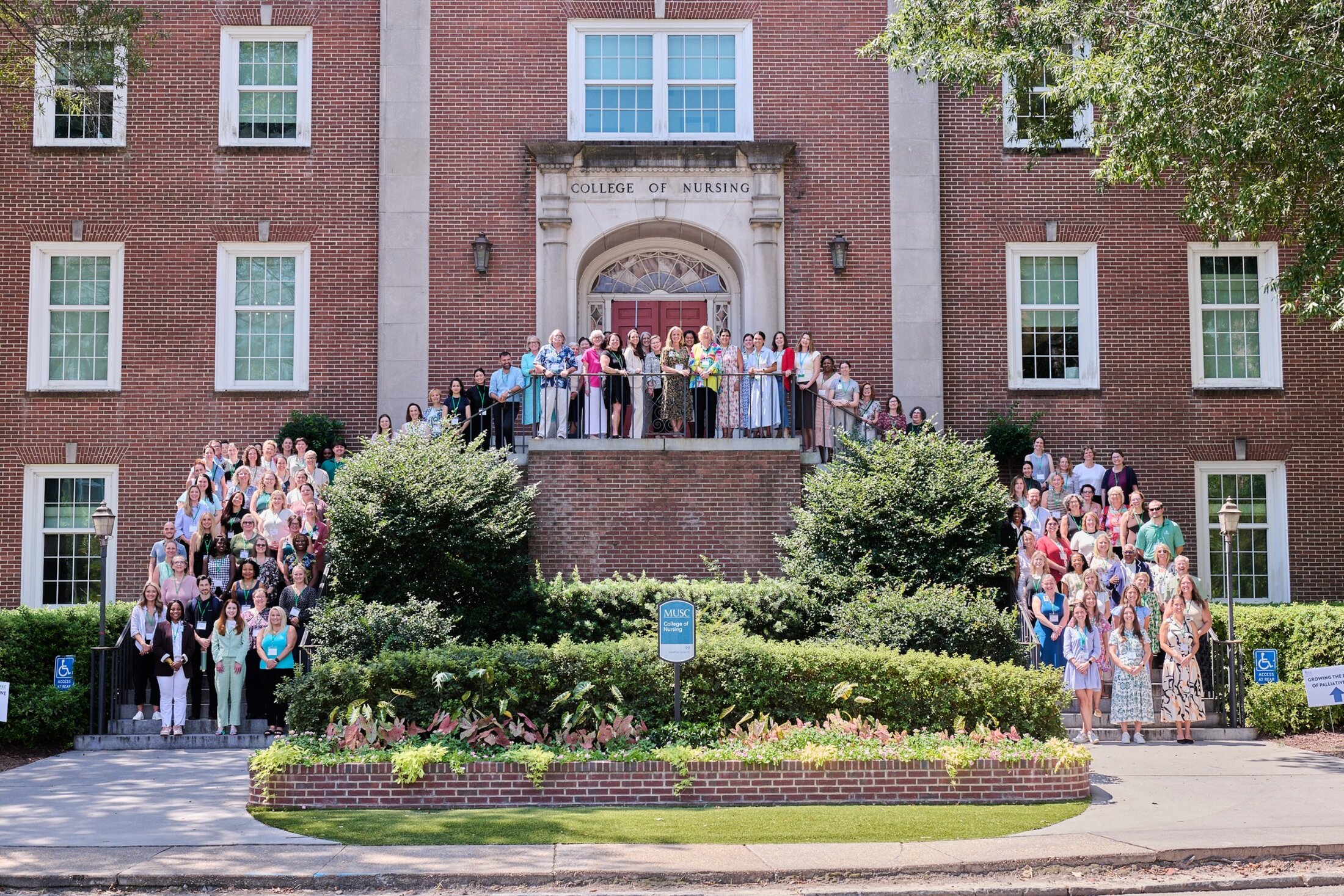 A horseshaped group of people standing in front of a brick building that says College of Nursing.