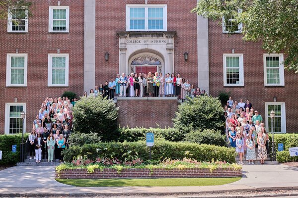 A horseshaped group of people standing in front of a brick building that says College of Nursing.