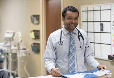 A physician looks up from paperwork in the work area behind exam rooms.