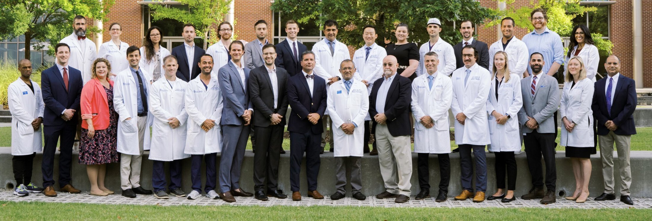 College of Medicine faculty and resident group photo taken outside with lab coats and blazers