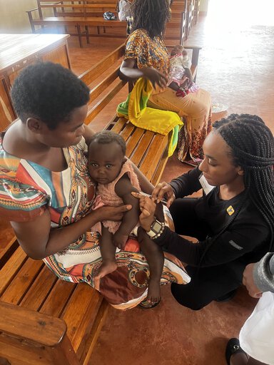 One woman holds a baby while another gives the baby a shot.