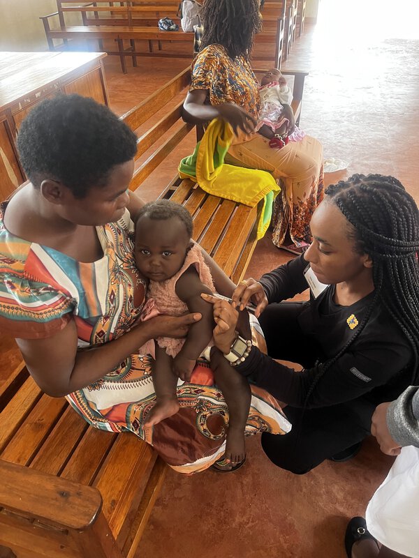 One woman holds a baby while another gives the baby a shot.