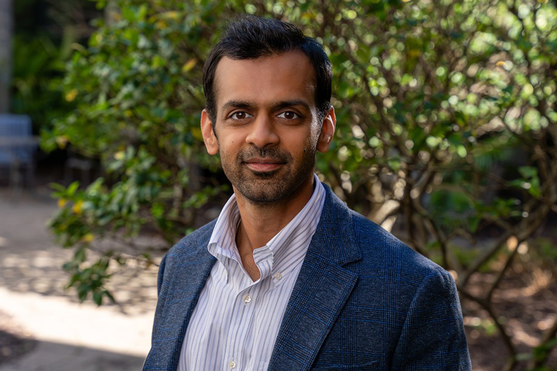 A researcher poses in casual business attire in a garden.