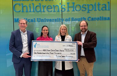 Four people in front of an MUSc Children's Hospital sign hold an oversized check from the Isabella Santos Foundation for $153,000.