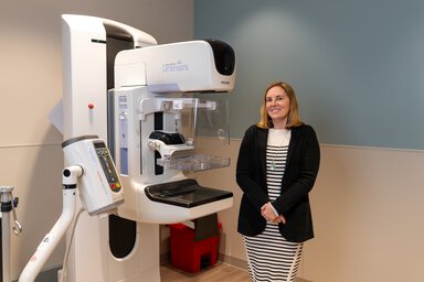 A woman poses next to a mammography machine.