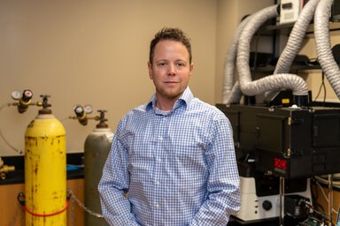 A cancer researcher poses in his lab surrounded by air tanks and a many-tubed machine.