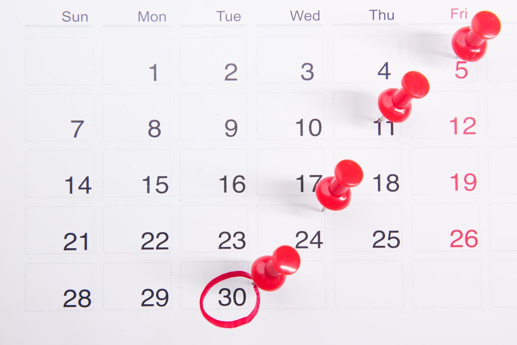 Calendar with important dates highlighted using red pushpins and a red circle around the 30th.