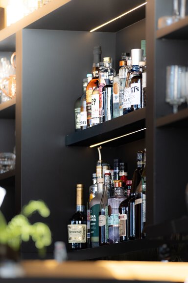 Two shelves of bottles of alcohol. They look like they are in a bar. The shelving is brown and black. The bottles are a variety of liquors. Hennessy label is most visible.