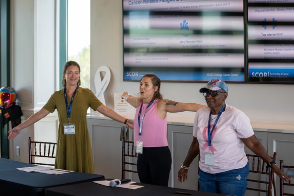 Three women stand with their arms held out at their sides leading an exercise.