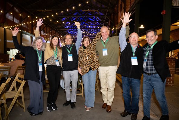 A diverse group of people gathered at a night time event, hands raised, indicating excitement.