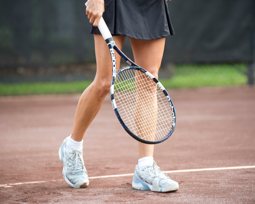 person holding tennis racket with racket pointing toward ground