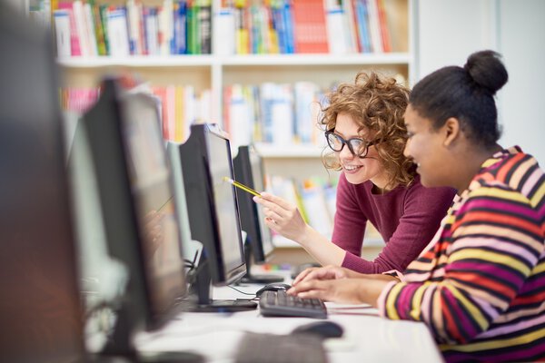 Two college students pointing at monitor and discussing presentation on computer together during computer course at college