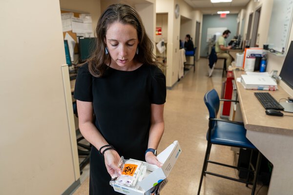 A doctor opens a testing kit at a hallway workstation outside of exam rooms.