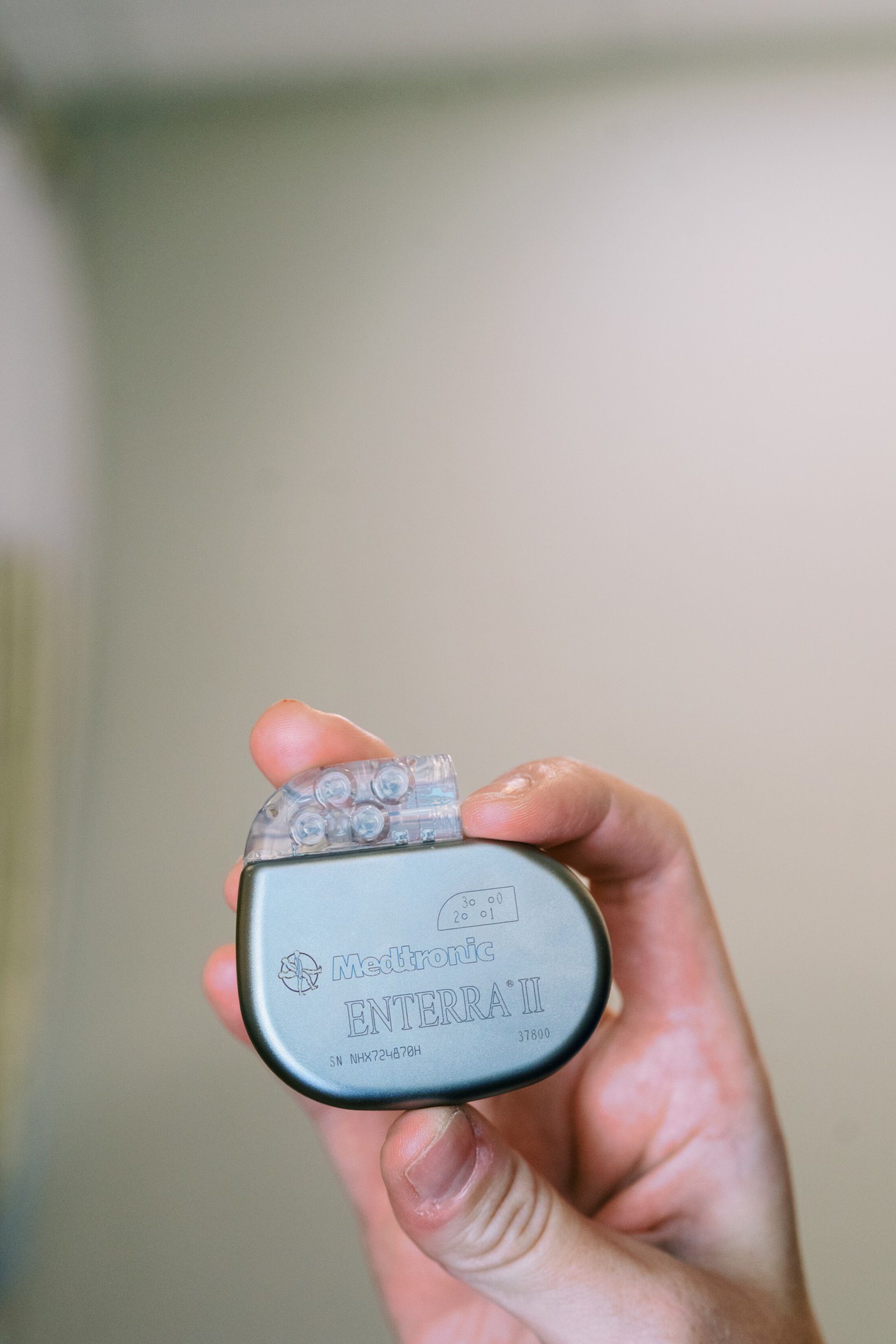 Right hand holding a small silver colored device that says Medtronic Enterra II.