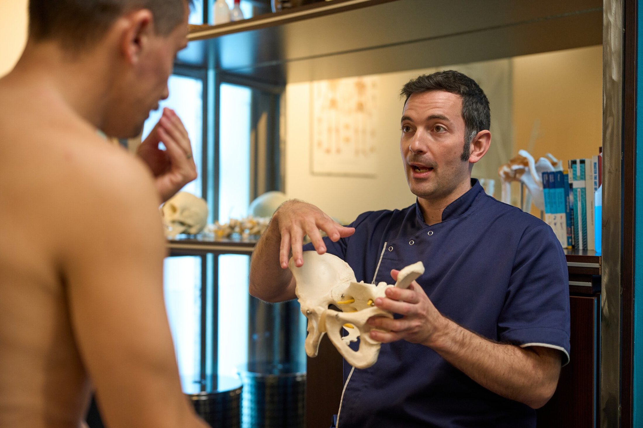 Physiotherapist showing a pelvis anatomical model to a patient during a consultation, explaining anatomy, posture, and common issues
