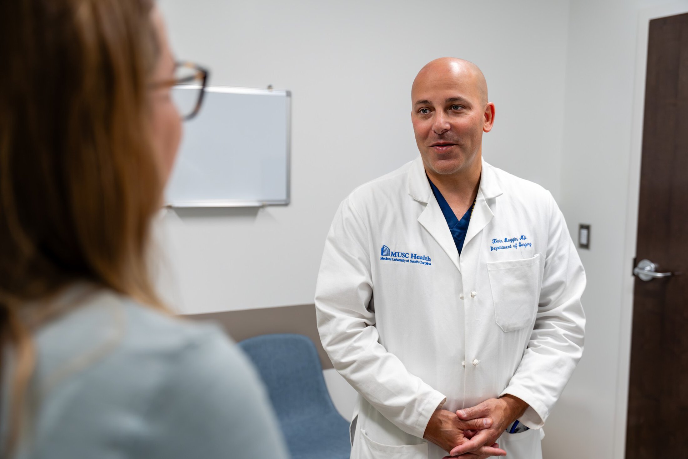 A doctor in a white coat listens intently to a nurse in clinic.