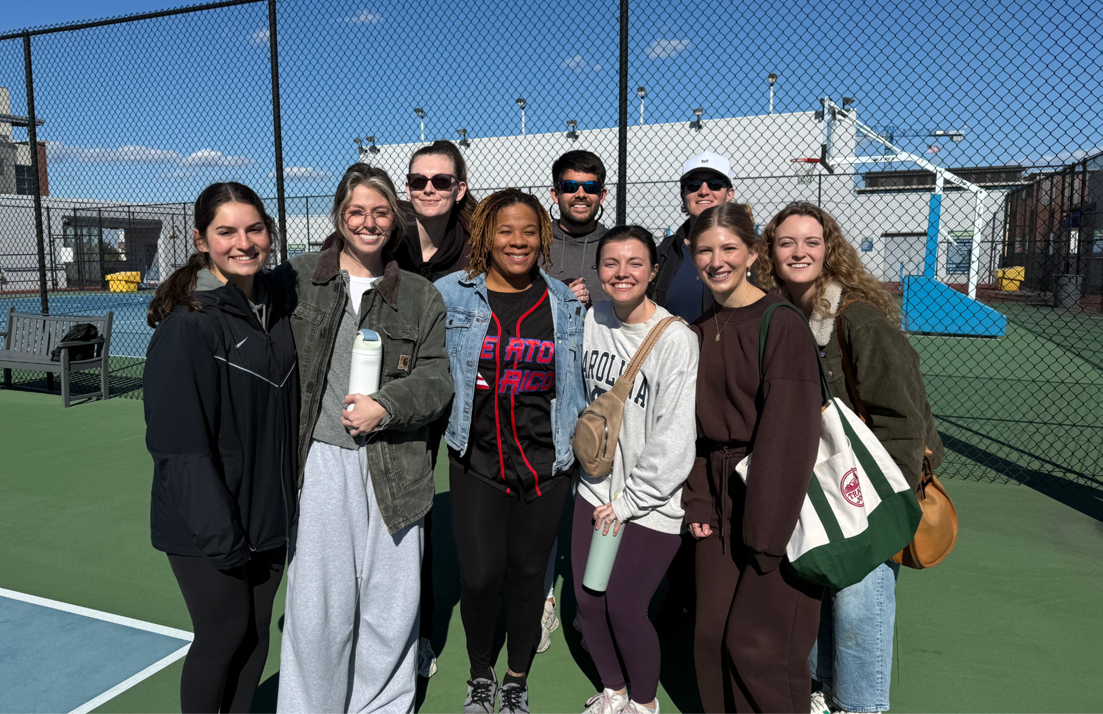 a group of people stand together on an outdoor pickle ball court.
