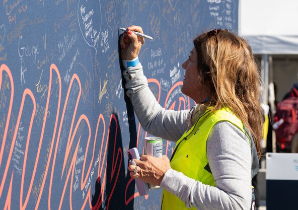 a woman writes a message on a large fabric sign intended for people to share why they ride in the Lowvelo fundraising bike ride