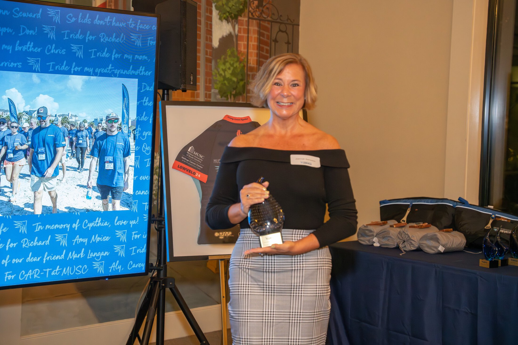 A woman smiles as she holds an award at an event.
