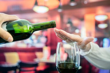 A woman holds her hand over a wine bottle indicating no more.