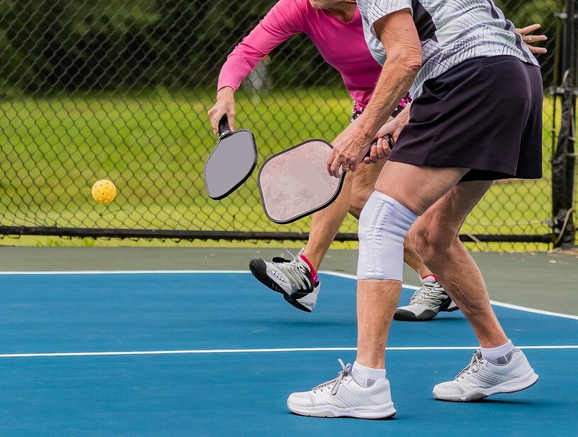 Women doubles pickleball players attempt to hit the ball