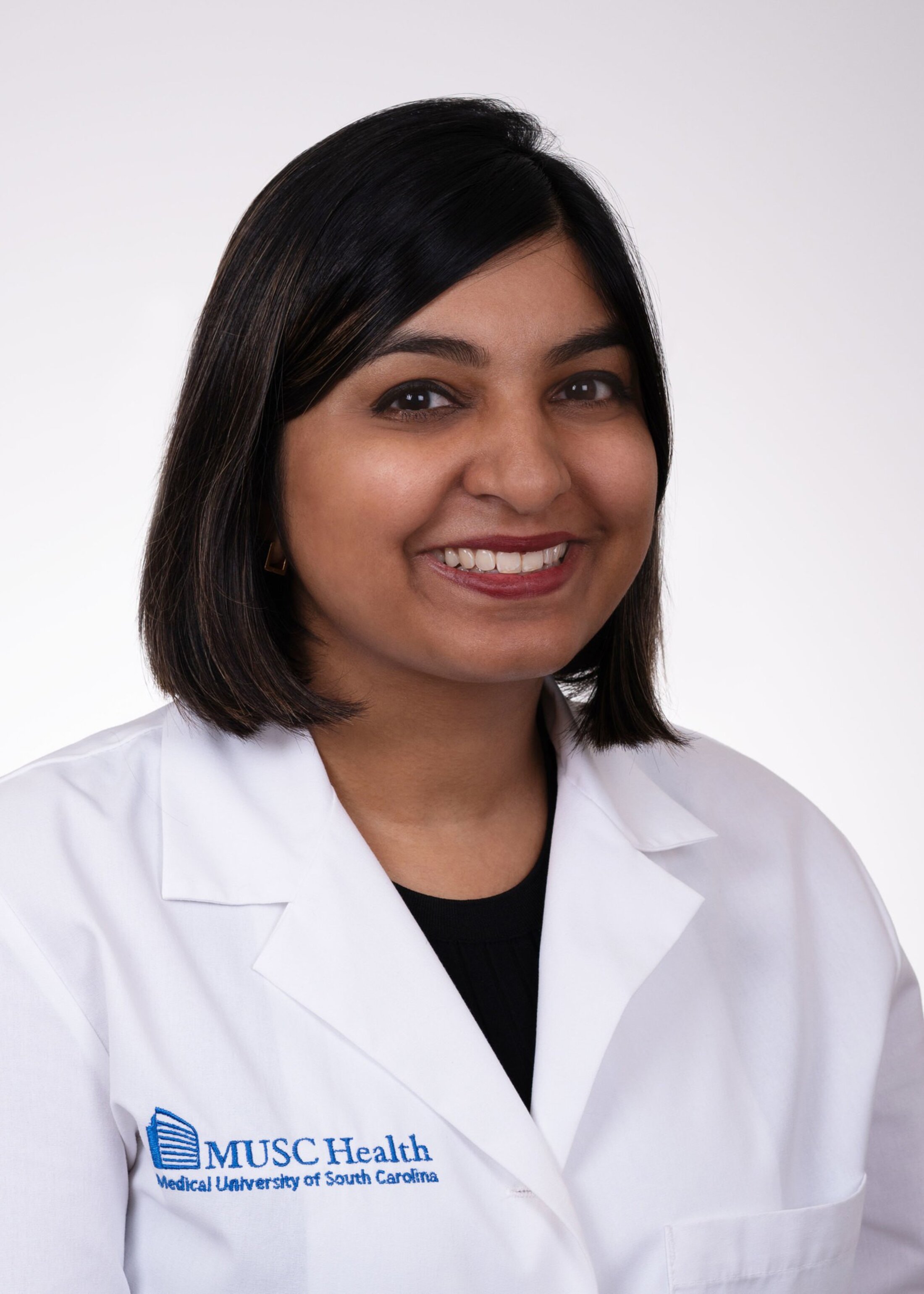 Woman with shoulder length dark hair smiles in a headshot. She is wearing a white doctor's coast with MUSC Health Medical University of South Carolina on the right side.
