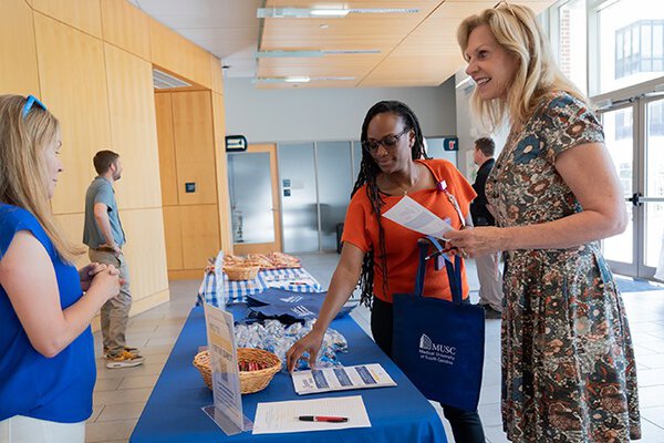 Three women meeting at a welcome table for a conference at MUSC