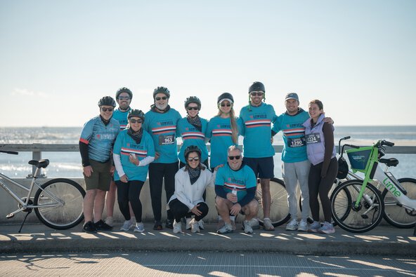 a large group stands together on the bridge over Breach Inlet with their bikes off to the side during a break in their Lowvelo ride