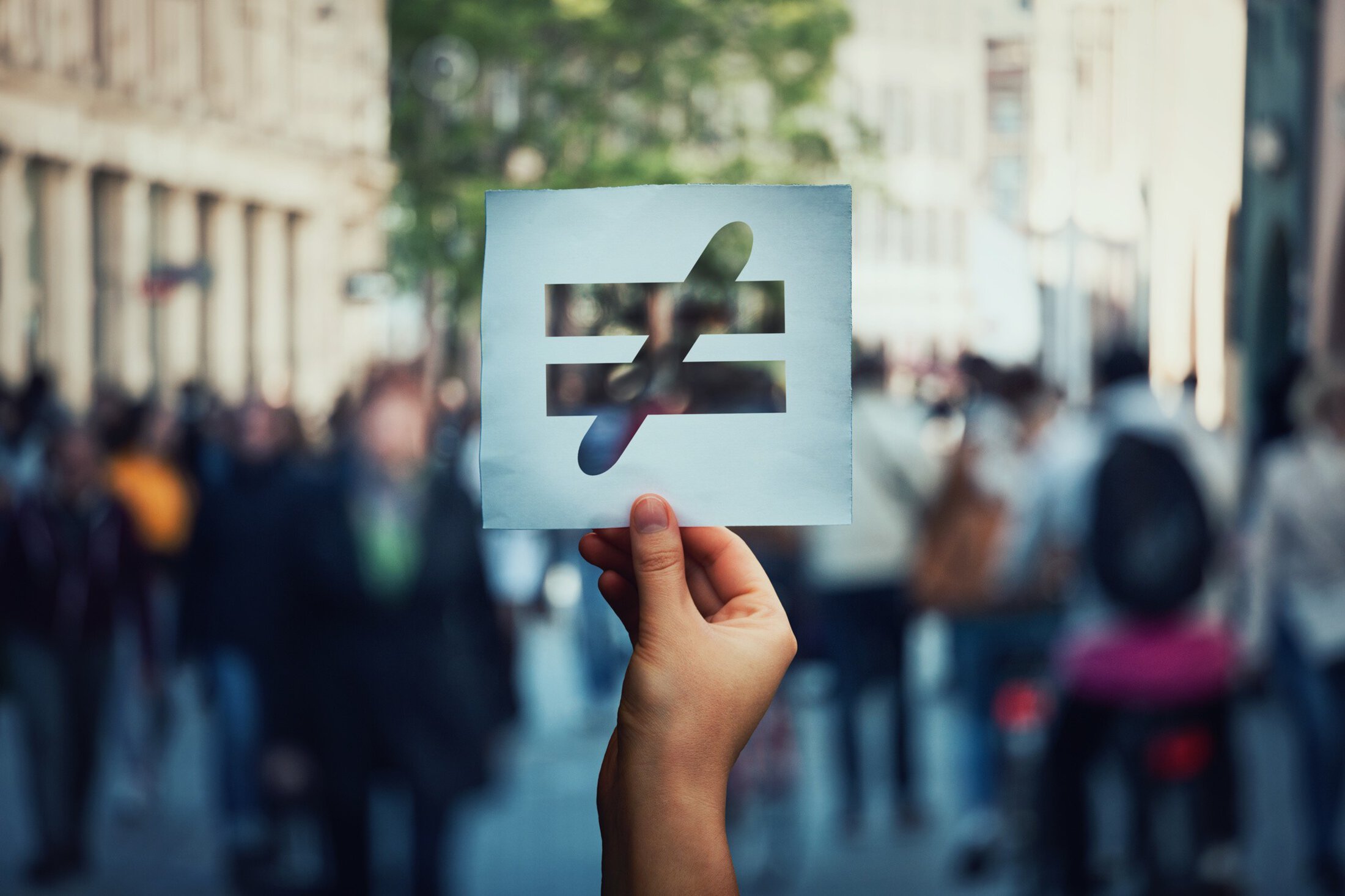 Hand holding up an unequal sign in front of a crowd