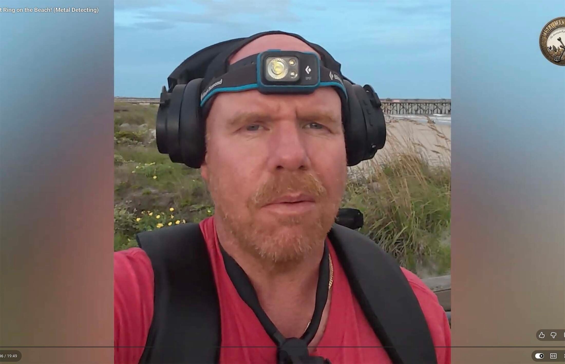 Man wearing a headlamp on the beach. He has a reddish beard and is wearing a red shirt with black straps crossing his shoulders.