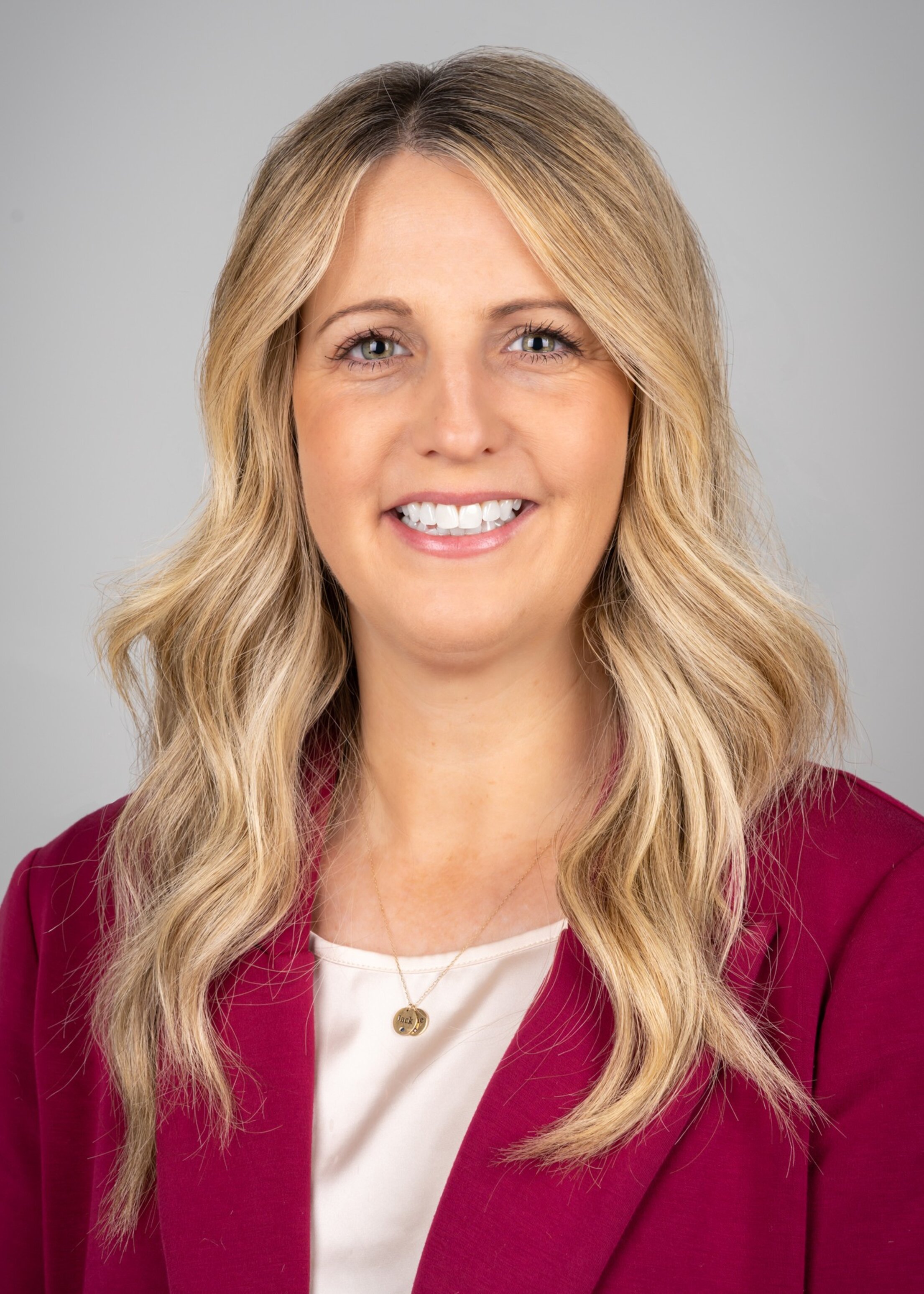 Headshot of woman with shoulder length blonde hair. She has large earrings and a pink and black polka-dot blouse.