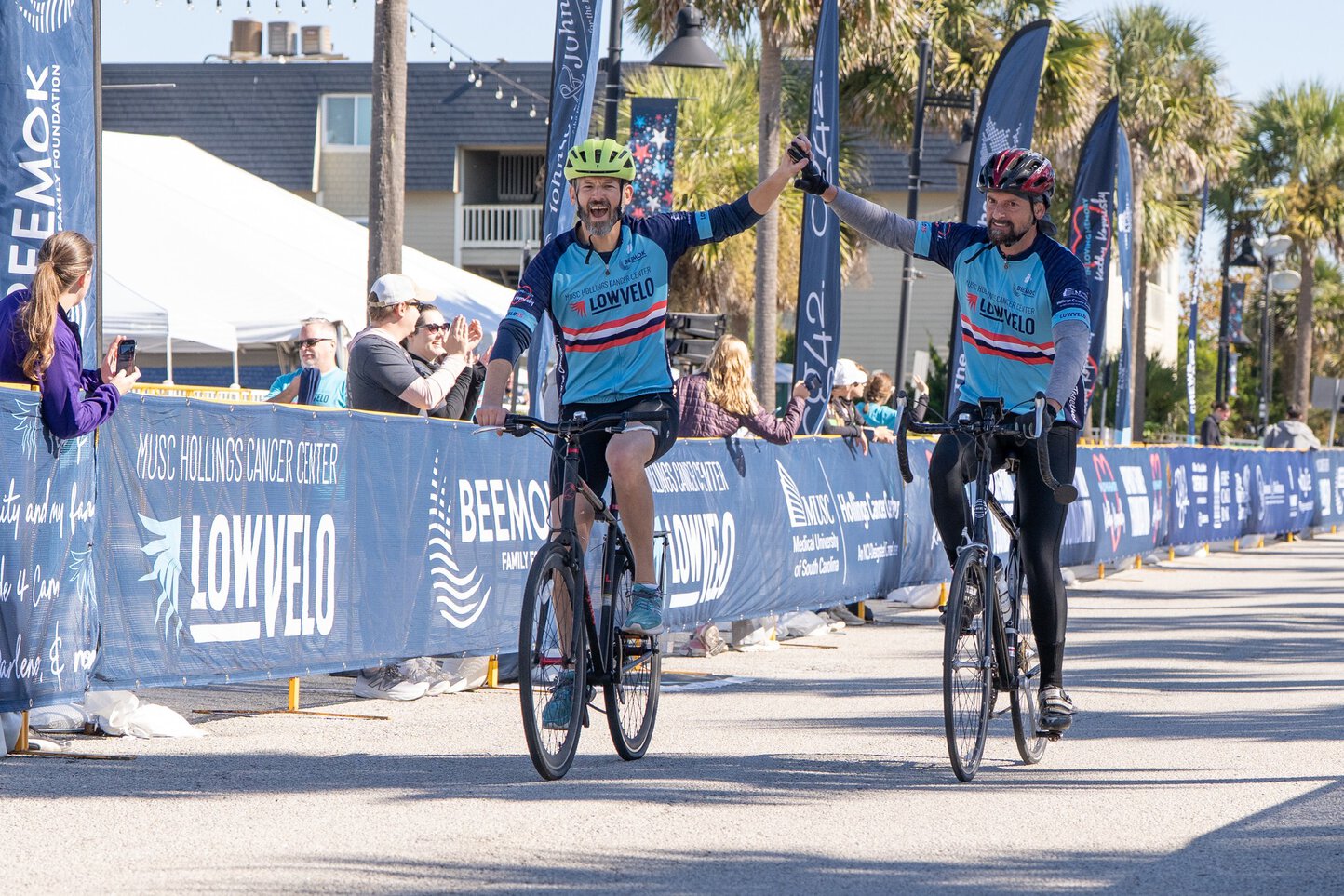 Two bicyclists join hands overhead as they cross a finish line at LOWVELO.