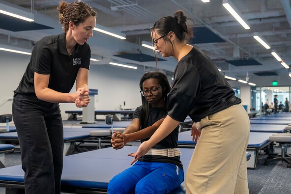 Woman instructs two female students through a rehabilitation technique