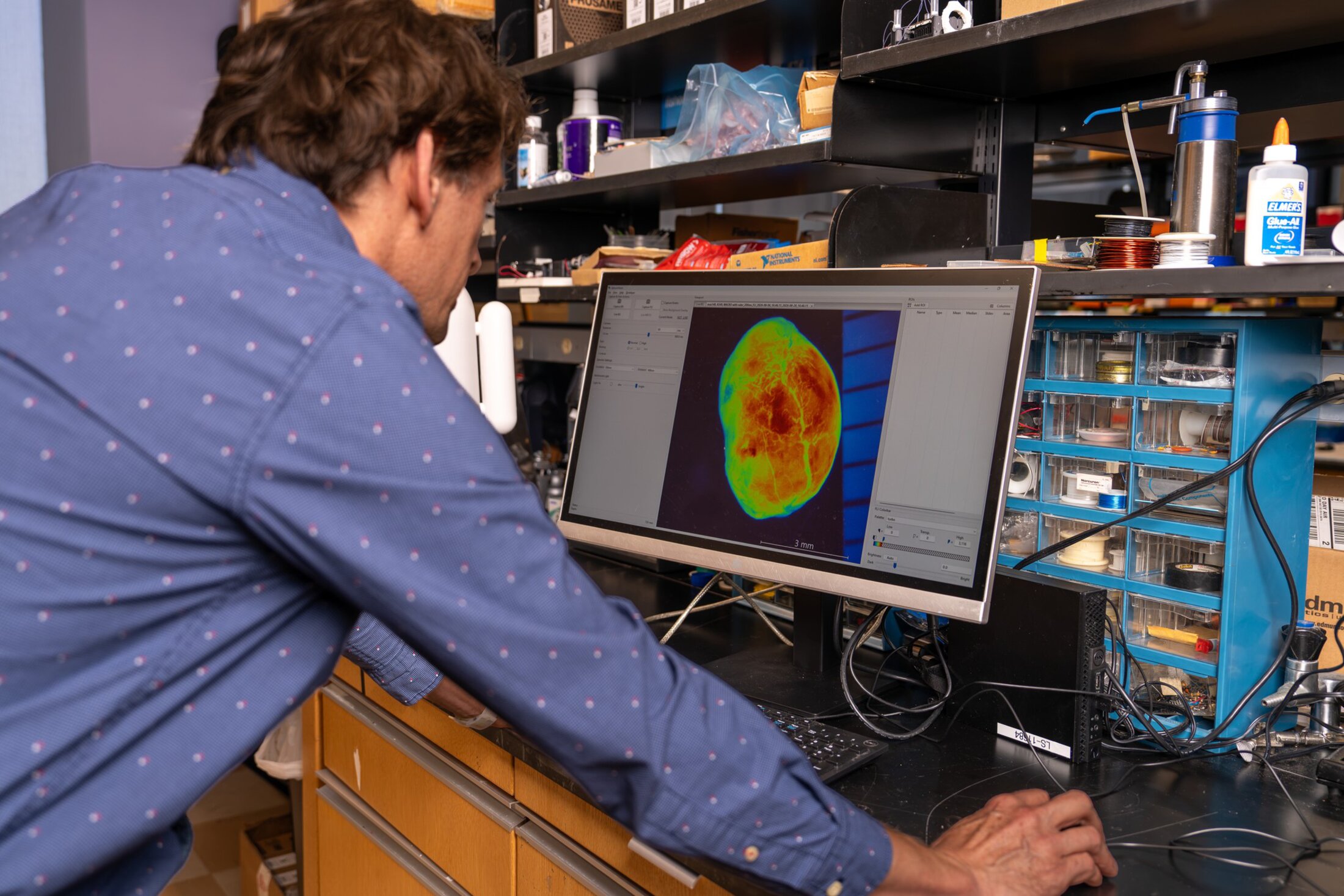 Dr. Haemmerich leans forward, resting his palms on the lab bench, to look at the image on a computer screen produced by the SphynxVision device.
