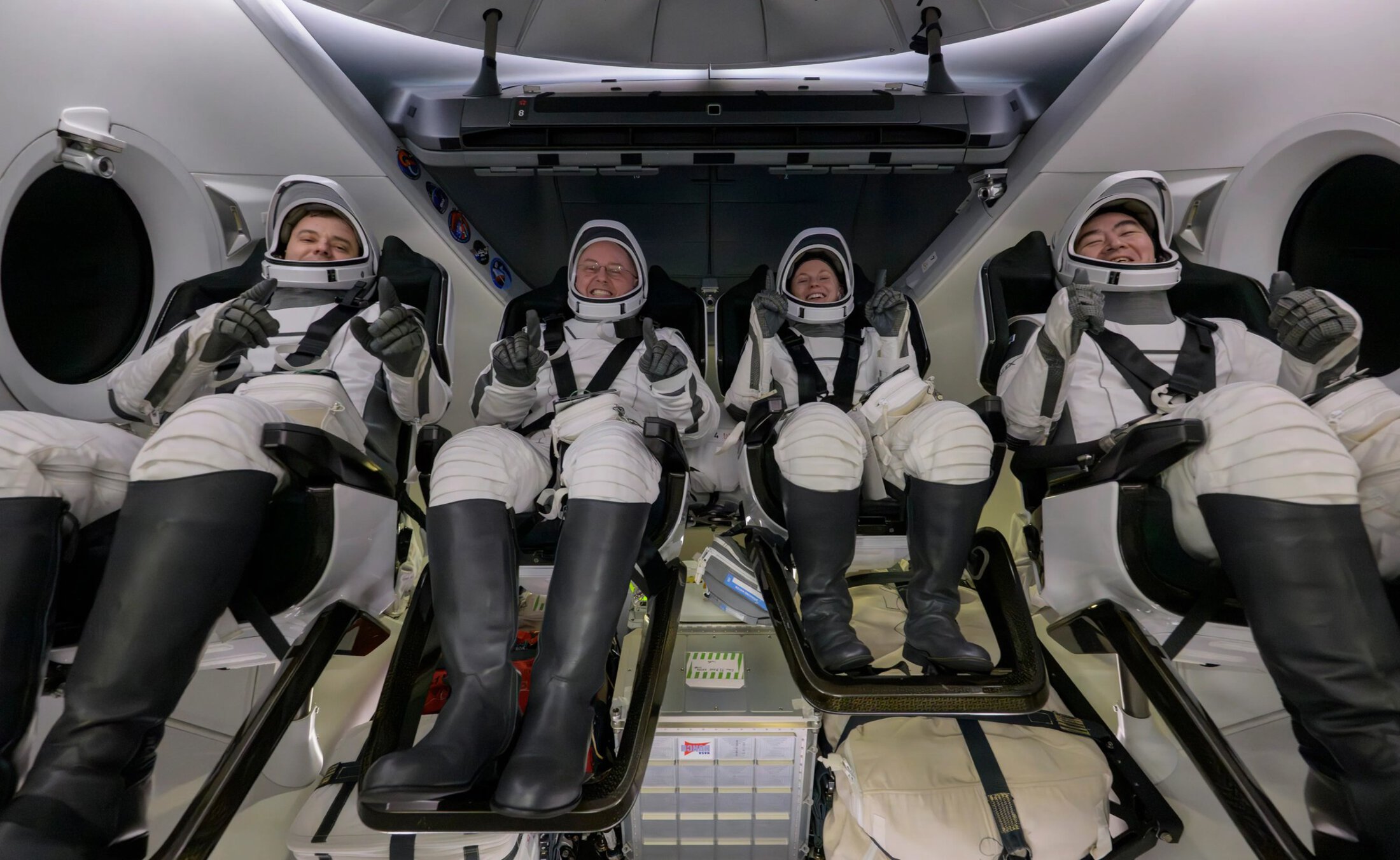 Four people in space suits give thumbs up to camera.