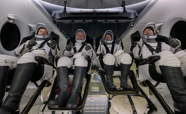 Four people in space suits give thumbs up to camera.