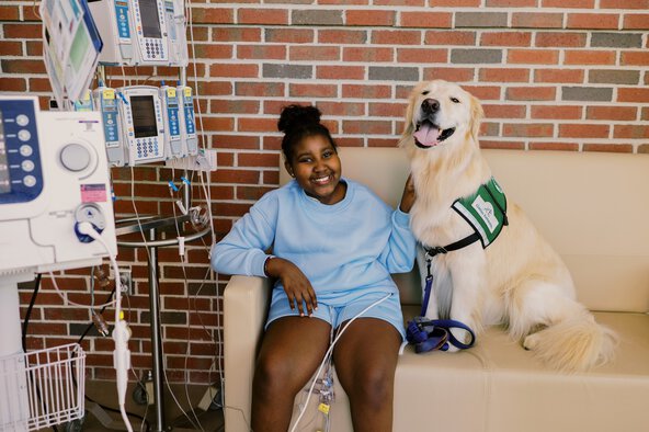 Golden Lab Therapy Dog sitting with a patient on a couch in the hospital