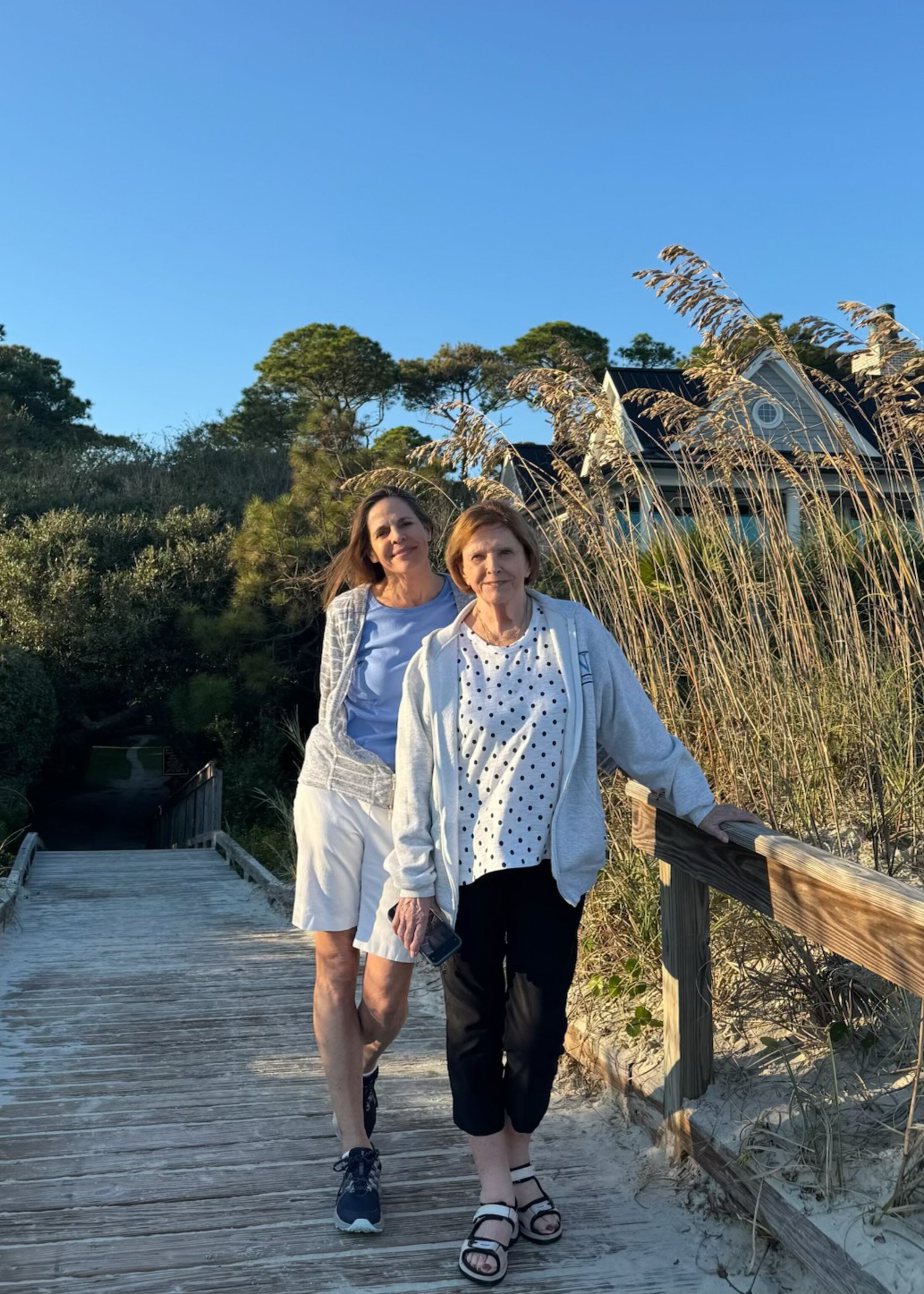 two women pose on a wooden walkway to the beach