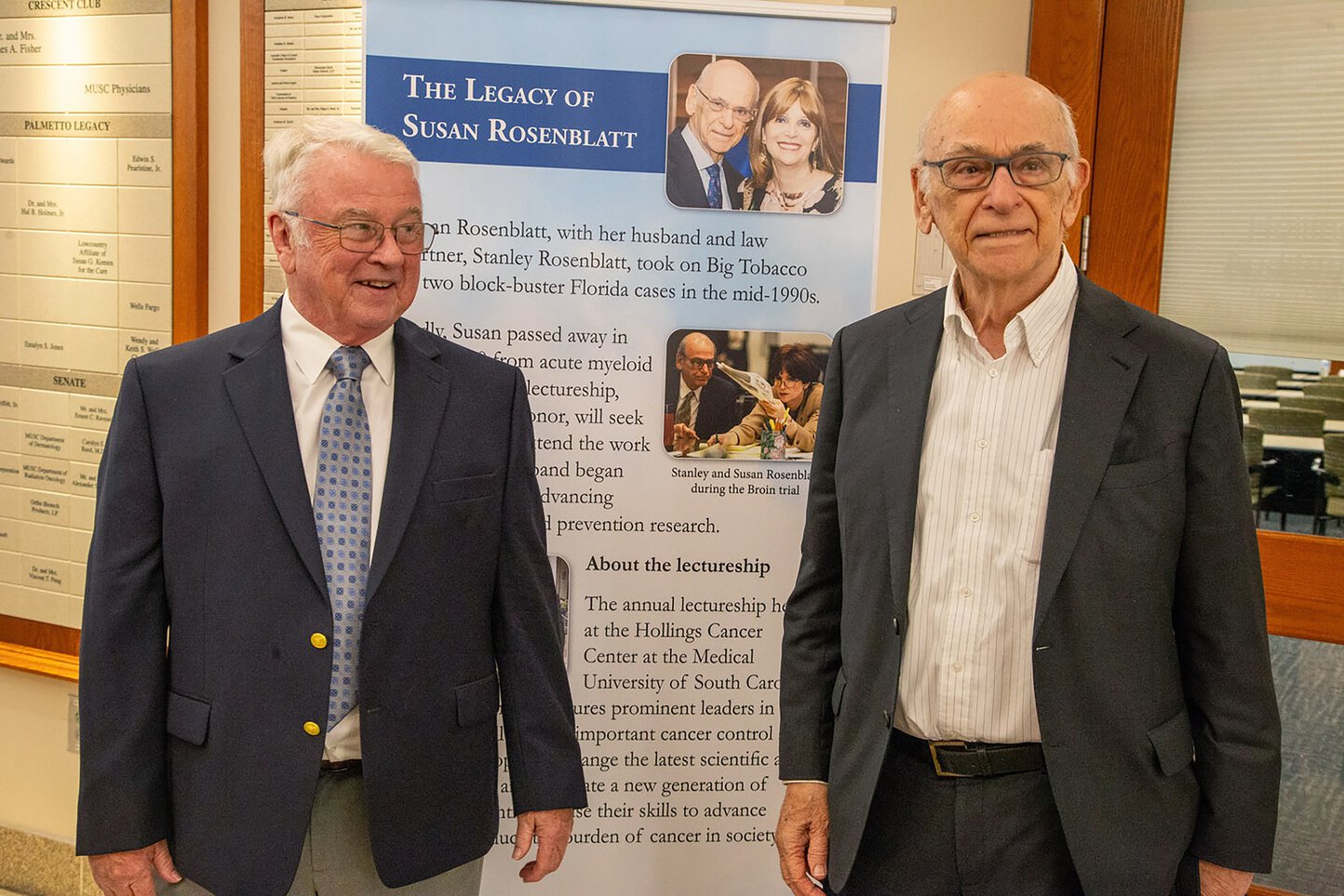 Two men smile in front of a poster describing the legacy of Susan Rosenblatt.