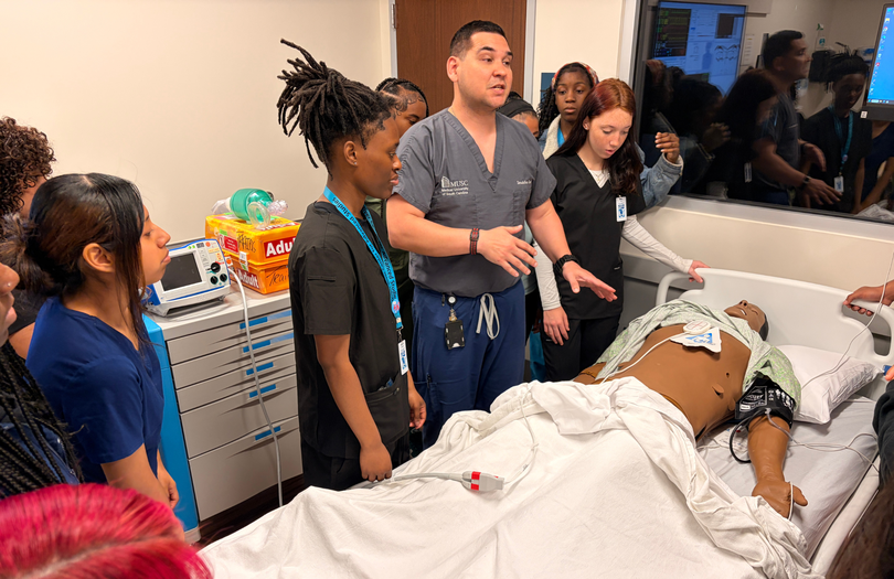 Staff member teaching high school students about medical training equipment.