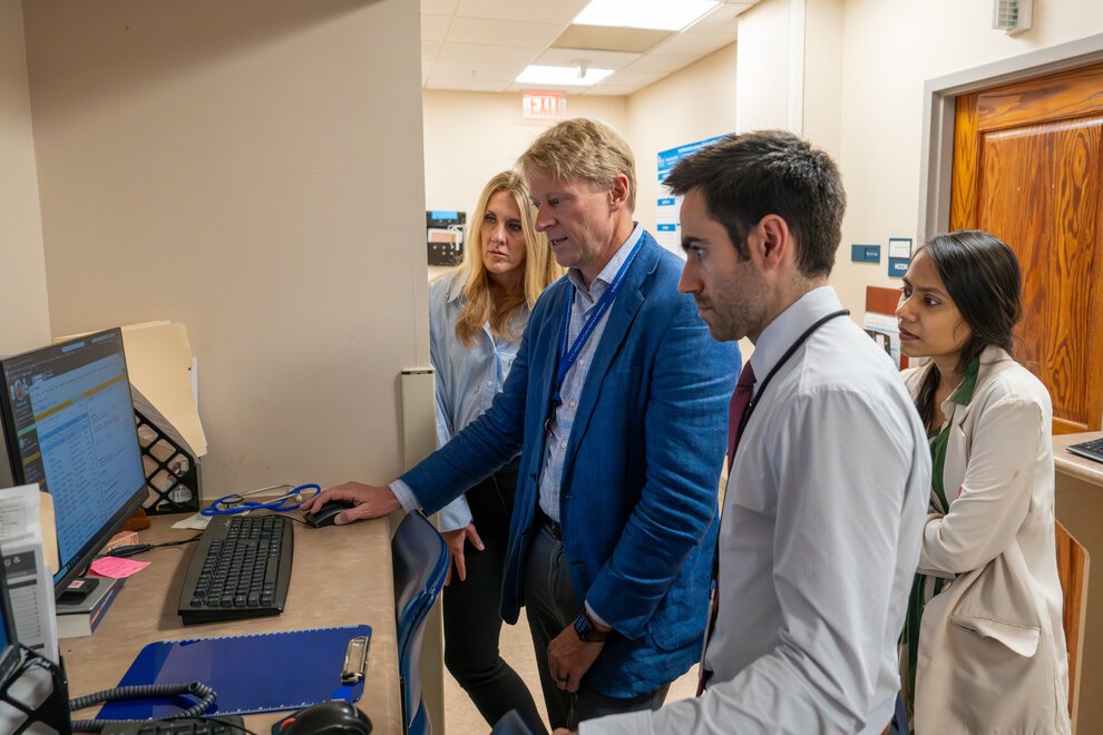 Doctors confer while looking at a computer screen in a workspace outside clinic exam rooms.