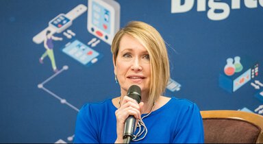Helen Caton-Peters speaks into a microphone during a panel discussion at the National Digital Health Strategy event, with a blue backdrop highlighting digital health and technology themes.